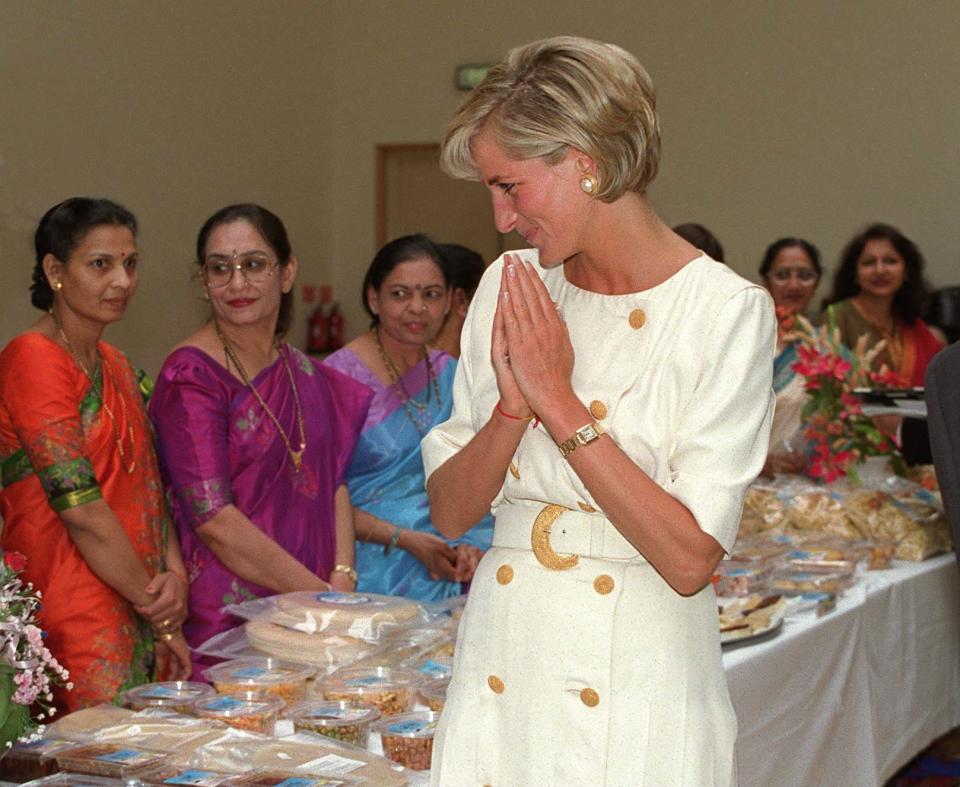 A picture of Princess Diana with her hands folded in a namaste post, wearing a long white dress.
