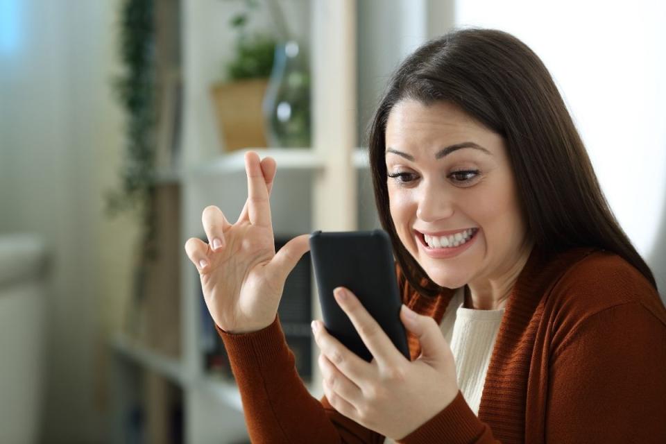 Woman checks Powerball results on phone with fingers crossed