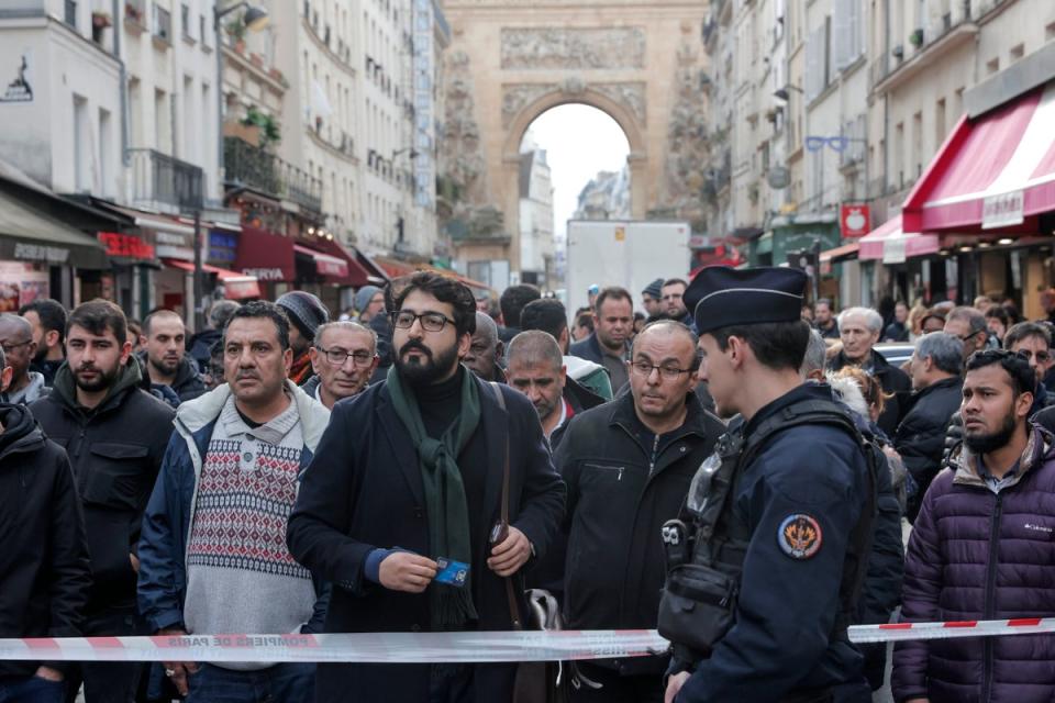 Bystanders gather behind the crime scene tape where a shooting took place in Paris (AP)