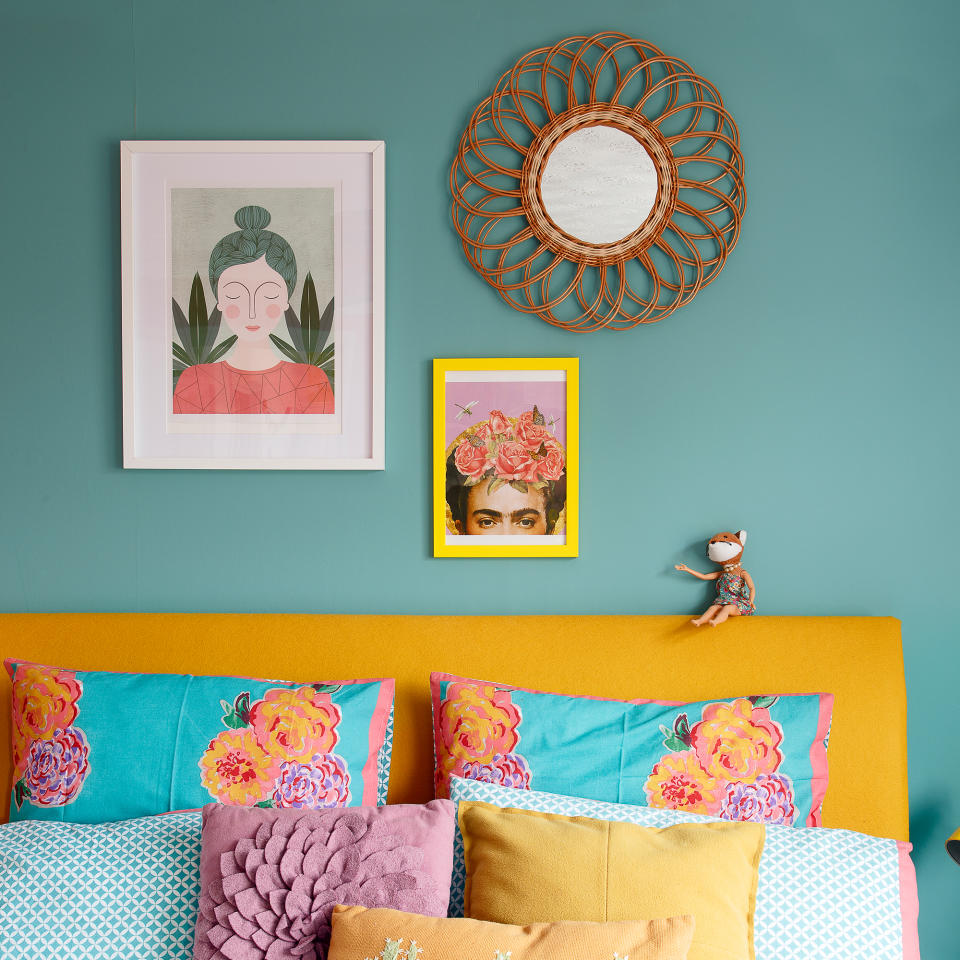 Turquoise bedroom with artwork, colourful cushions and yellow headboard