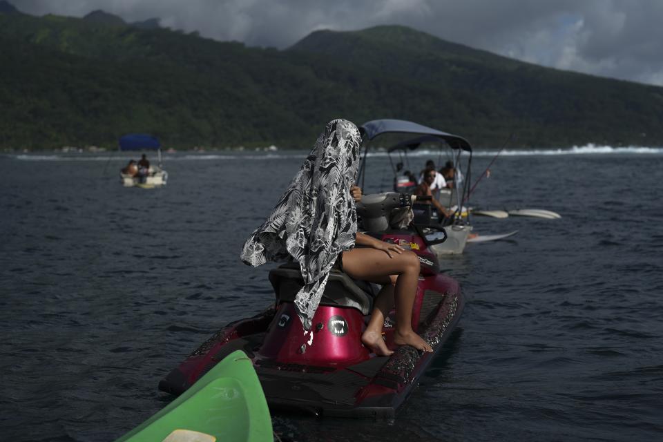 A woman shelters from the sun as she watches surfers catching waves in Vairao, Tahiti, French Polynesia, Monday, Jan. 15, 2024. (AP Photo/Daniel Cole)