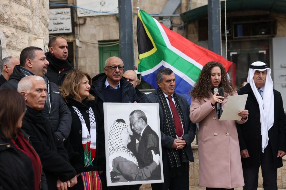 A Palestinian man holds a portrait of late Palestine Liberation Organisation (PLO) leader Yasser Arafat and South Africa's anti-apartheid icon Nelson Mandela before raising the South African national flag outside the municipality building in Bethlehem in the occupied West Bank on January 12, 2024.