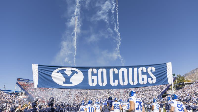 The BYU marching band hold up a banner as players run under it during a football game at LaVell Edwards Stadium in Provo on Saturday, Oct. 15, 2022.