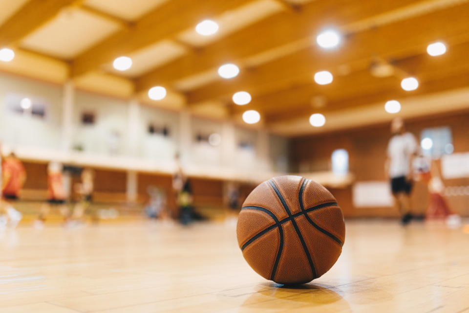 Basketball training game background.  Basketball on wooden court floor close up with blurred players playing basketball in background