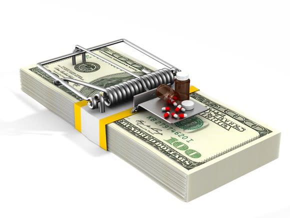 Stack of money arranged like a mousetrap with medicine as bait.