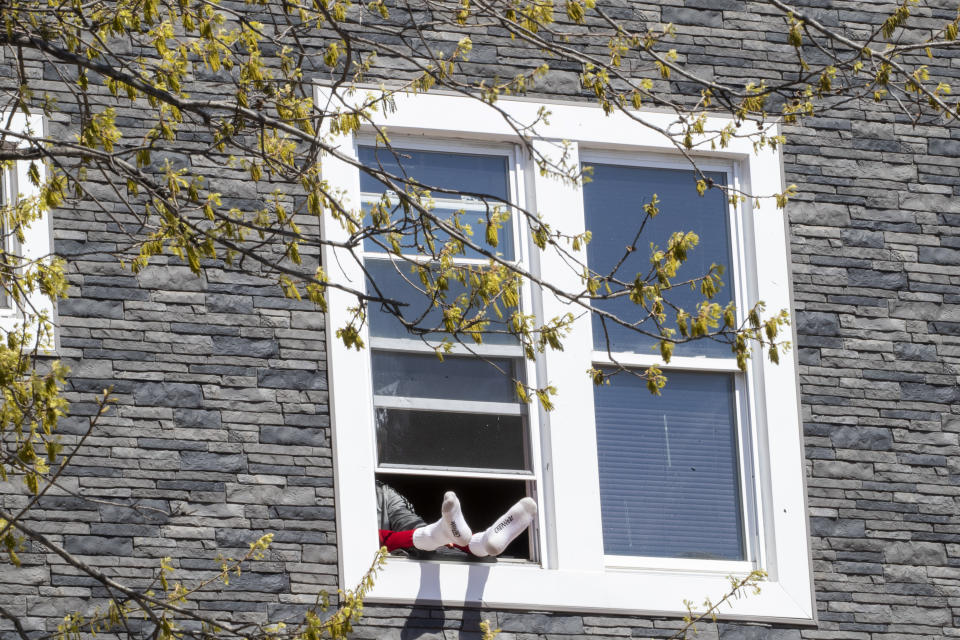 A man sits with his feet hanging out the window while self isolating during the coronavirus pandemic, Saturday, April 11, 2020, in the Flatbush neighborhood of the Brooklyn borough of New York. The new coronavirus causes mild or moderate symptoms for most people, but for some, especially older adults and people with existing health problems, it can cause more severe illness or death. (AP Photo/Mary Altaffer)