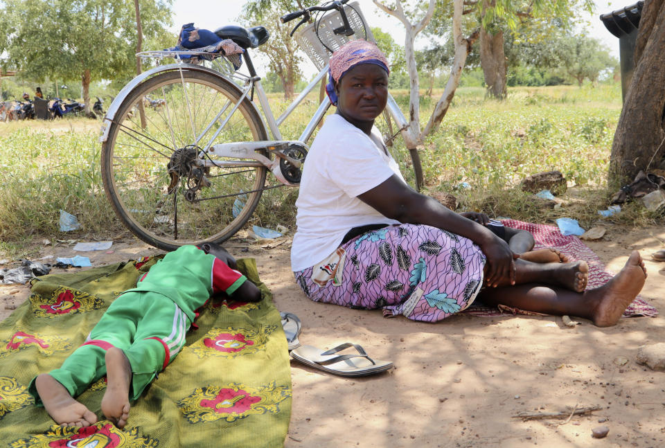 A woman sits on the ground beside a sleeping child, outside a small clinic in Gampela village on the outskirts of Burkina Faso's capital, Ouagadougou, Saturday Oct. 10, 2020. People sometimes wait up to four hours to get medical help. The public health clinic responsible for serving approximately 11,000 people, did not have a working fridge for almost a year. The vaccine cold chain hurdle is just the latest disparity of the pandemic weighted against the poor, who more often live and work in crowded conditions that allow the virus to spread, have little access to medical oxygen vital to COVID-19 treatment, and whose health systems lack labs, supplies or technicians to carry out large-scale testing. (AP Photo/Sam Mednick)