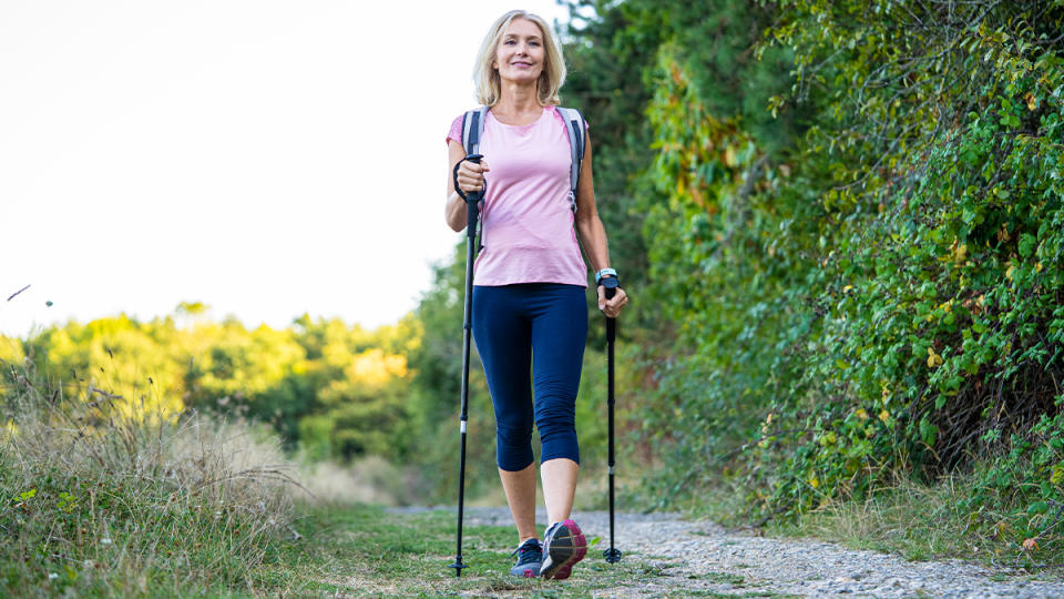 Mature woman walking down a path outside using walking poles