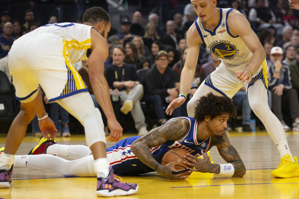 Philadelphia 76ers guard Kelly Oubre Jr., center, loses his footing between Golden State Warriors guards Stephen Curry, left, and Brandin Podziemski (2) during the first half of an NBA basketball game, Tuesday, Jan. 30, 2024, in San Francisco. (AP Photo/D. Ross Cameron)