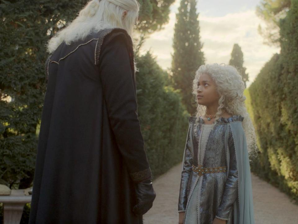 A young girl (11 years old) with curly white hair and a blue gown standing in front of a middle-aged man.