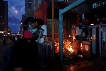 An anti-government protester walks past a burning barrier outside Mongkok MTR station during a demonstration following a government's ban on face masks under emergency law, in Hong Kong