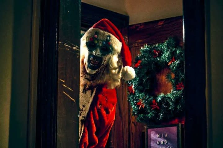 A bloody clown dressed like Santa Claus stands in the doorframe.