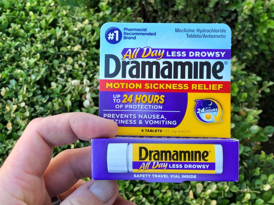 Hand holding purple and yellow container of dramamine