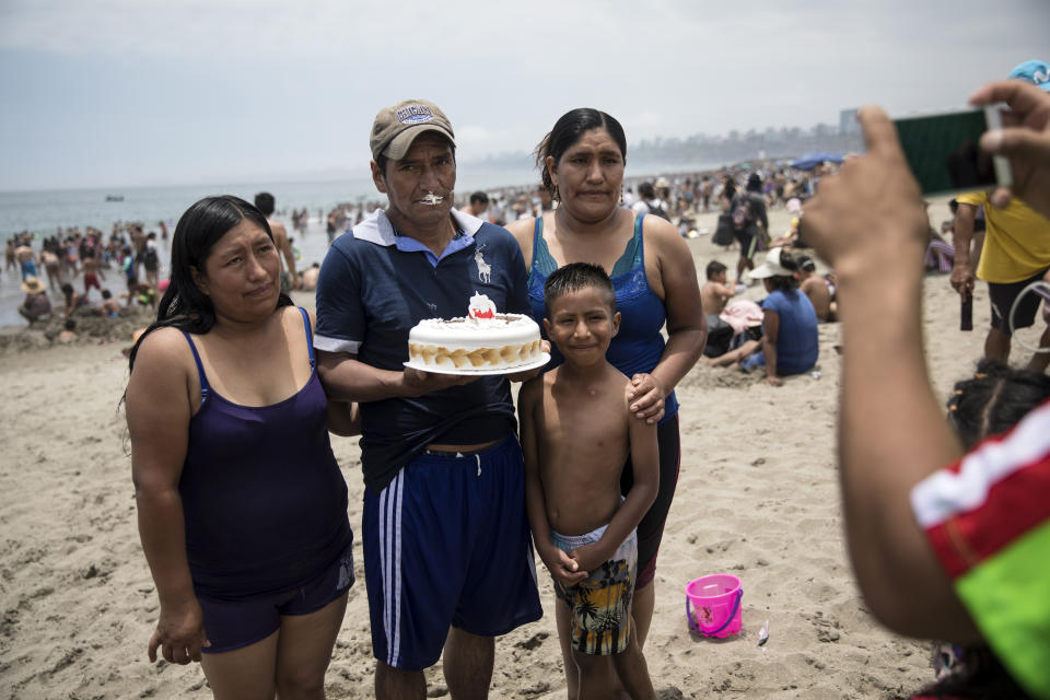 In this Feb. 23, 2020 photo, a man, holding his birthday cake, poses for a photo with his family on the shore of Agua Dulce beach in Lima, Peru. The half-mile-long (kilometer-long) strip of grayish-brown sand 12 miles (20 kilometers south of central Lima) is a haven for the working classes, a place where visitors from the Andean highlands first dip a toe in the sea. (AP Photo/Rodrigo Abd)