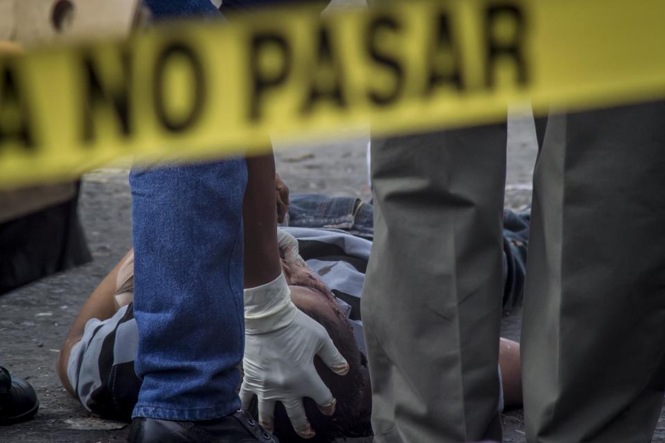 A forensic workers checks the body of a victim of a shootout between private security guards and gang members, at the central market in San Salvador, El Salvador, Wednesday, March 15, 2017. At least 30 people, mostly gang members, died in the last 24 hours in El Salvador on one of the most violent days so far this year. (AP Photo/Salvador Melendez)