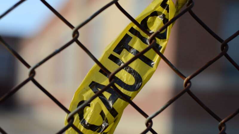 A piece of yellow CAUTION tape in a chain link fence.