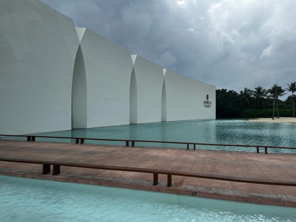 A wooden pathway over a pool of water leading to a white building with arches