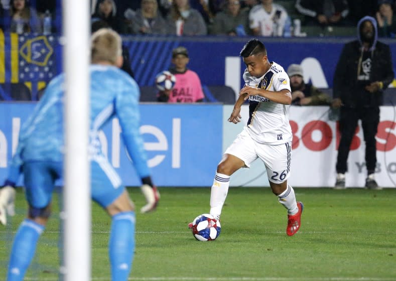 In this Saturday, March 2, 2019 photo, LA Galaxy midfielder Efrain Alvarez, right, prepares to kick against Sporting Kansas City goalkeeper Adrian Zendejas during an MLS soccer match in Carson, Calif. U.S. coach Gregg Berhalter is monitoring Efrain Alvarez, the 16-year-old midfielder who had an assist in his LA Galaxy debut last weekend and is eligible to play for both the Americans and Mexico.(AP Photo/Ringo H.W. Chiu)