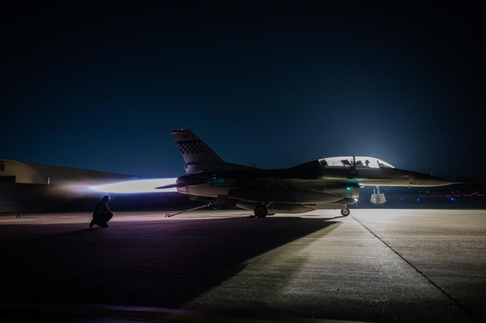 An F-16 fighter jet at on the tarmac at an air base at night.