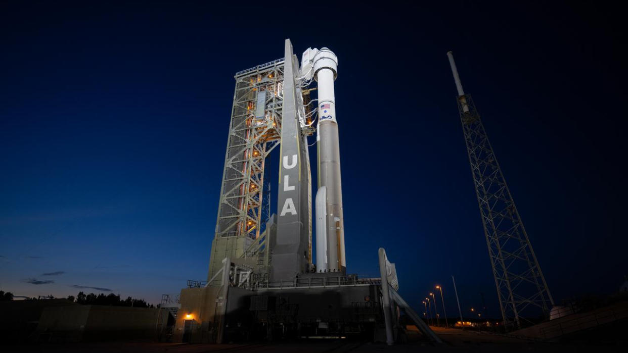  A large white rocket sits vertical on a launch pad at night. 