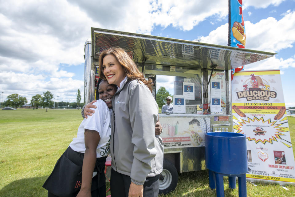 Michigan Gov. Gretchen Whitmer, right, gets a hug from Shante Rice, an employee at the hot dog stand Delicious Dogs before a press conference on Belle Isle in Detroit, on Tuesday, June 22, 2021, announcing the end of COVID restrictions in the state. After facing 15 months of capacity restrictions and being hit by the country’s worst surge of coronavirus infections this spring, restaurants, entertainment businesses and other venues can operate at 100% occupancy starting Tuesday. (David Guralnick/Detroit News via AP)