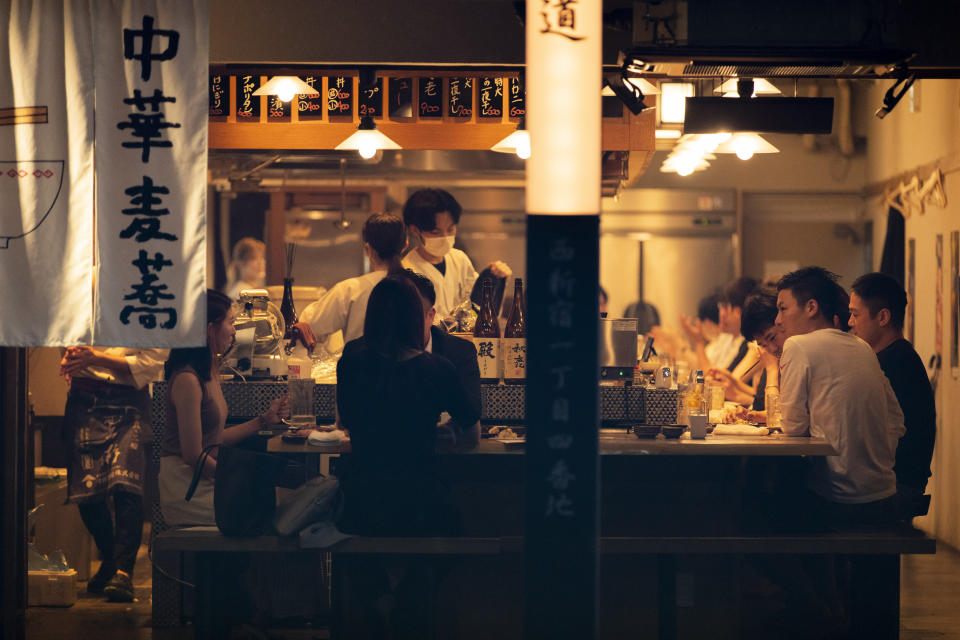 FILE - In this July 9, 2021, file photo, people eat and drink at a restaurant in the evening in Tokyo before a state of emergency being imposed on July 12, 2021 in the capital. Japan has resisted lockdowns even as cases have risen to record levels. It has instead relied on widespread mask use and emphasized its vaccination campaign, which began slowly but has accelerated to more than 1 million shots a day. (AP Photo/Hiro Komae, File)