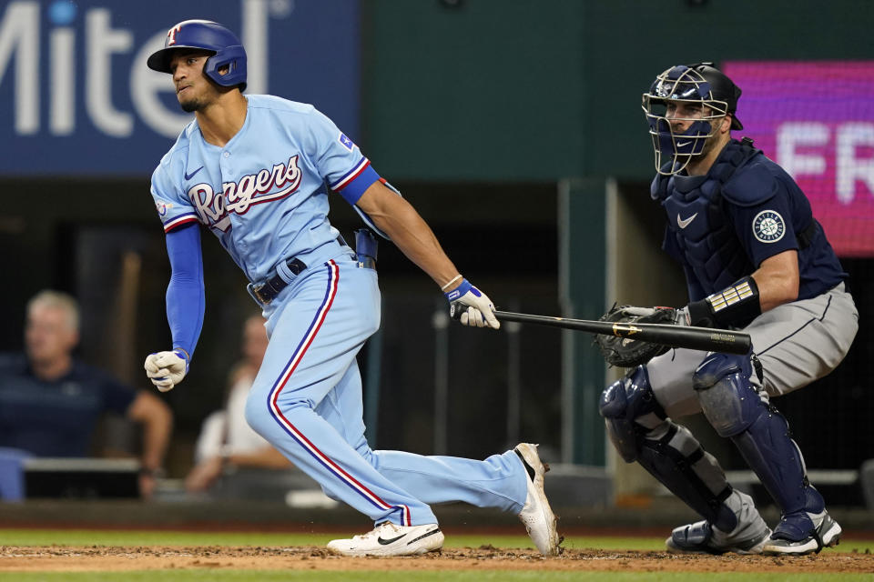 Texas Rangers' Bubba Thompson, left, and Seattle Mariners catcher Curt Casali (5) watch Thompson's single that drove in two runs during the fourth inning of a baseball game in Arlington, Texas, Sunday, Aug. 14, 2022. Rangers' Meibrys Viloria and Nathaniel Lowe (30) scored on the play. (AP Photo/LM Otero)