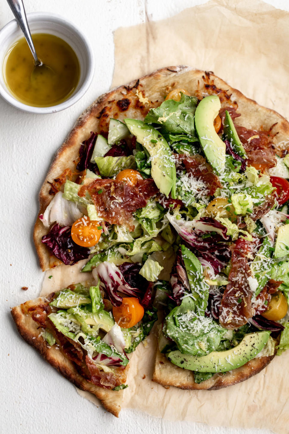 A pizza topped with lettuce, tomato, avocado, and proscuitto.