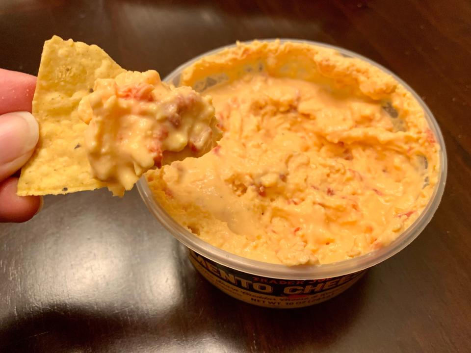 chip dipping in trader joe's pimento cheese dip on wood table