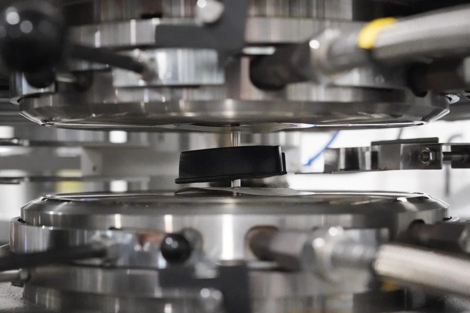 A hockey puck-shaped blob, called a "biscuit" and made of heated vinyl pellets, is set into a press to be formed into a vinyl record at the United Record Pressing facility Thursday, June 23, 2022, in Nashville, Tenn. The arrival of the compact disc nearly killed off record albums. Four decades later, with resuscitated record album sales producing double-digit growth, manufacturers are rapidly rebuilding an industry to keep pace with sales that topped $1 billion last year. (AP Photo/Mark Humphrey)