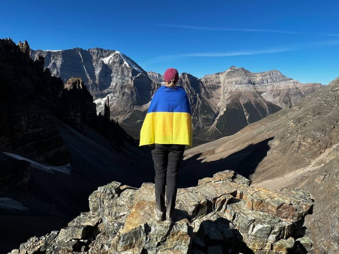 Valeriia Marchuk, seen here on a hike in the Canadian Rockies with a Ukrainian flag, arrived in Calgary in 2022 after her home was destroyed in a Russian airstrike on Kyiv.  (Valeriia Marchuk - image credit)