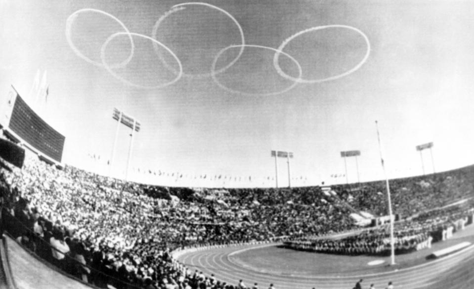 FILE - In this Oct. 10, 1964, file photo, vapor trails from Japanese Self-Defense Force jets from the Olympic emblem of five rings above the National Stadium in Tokyo for the official opening of the XVIII Olympiad, first even held in Asia. The famous 1964 Tokyo Olympics highlighted Japan’s resiliency. It was a prospering country that was showing off bullet trains, transistor radios, and a restored reputation just 19 years after devastating defeat in World War II. Now Japan and Tokyo are on display again, attempting to stage the postponed 2020 Tokyo Olympics in the midst of a once-in-a century pandemic. (AP Photo, File)