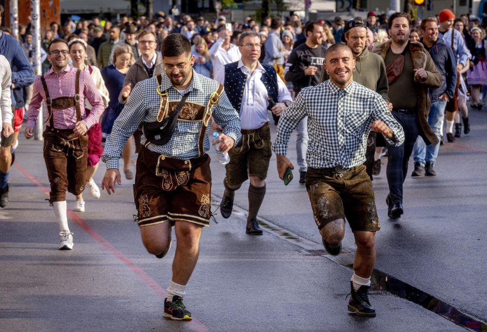 People run onto the festival ground on the opening day of the 187th Oktoberfest beer festival in Munich, Germany, Saturday, Sept. 17, 2022. Oktoberfest is back in Germany after two years of pandemic cancellations, the same bicep-challenging beer mugs, fat-dripping pork knuckles, pretzels the size of dinner plates, men in leather shorts and women in cleavage-baring traditional dresses. (AP Photo/Michael Probst)