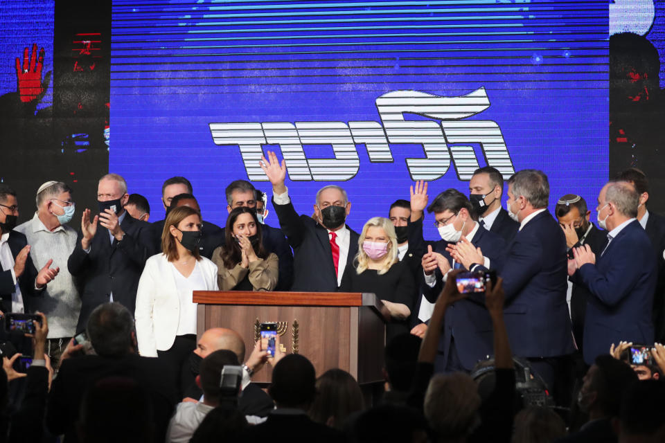 Israeli Prime Minister Benjamin Netanyahu, center, wearing a protective face mask, waves after delivering a speech to supporters following the announcement of exit polls of the Israeli parliamentary elections at his party's headquarters in Jerusalem, Wednesday, March. 24, 2021. (AP Photo/Ariel Schalit)