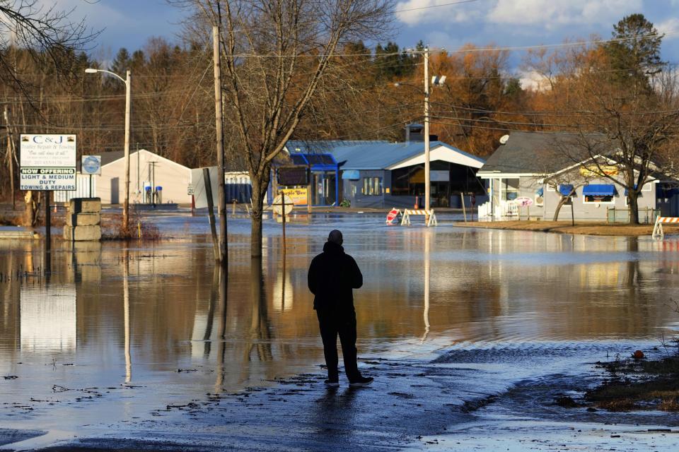 A man pauses at the edge of a flooded road near the Kennebec River, Tuesday, Dec. 19, 2023, in Fairfield, Maine. A severe storm on Monday flooded rivers and knocked out power to hundreds of thousands. (AP Photo/Robert F. Bukaty)