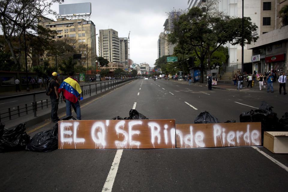 People gather next to a barricade with a sign that reads in Spanish: "He who gives up, loses" in Caracas, Venezuela, Monday, Feb. 24, 2014. Since Feb. 12, opponents of President Nicolas Maduro have been staging countrywide protests that the government says have resulted in scores of deaths and more than one hundred injuries. The demonstrators blame Maduro's administration for the country's high crime rate and economic troubles. (AP Photo/Rodrigo Abd)