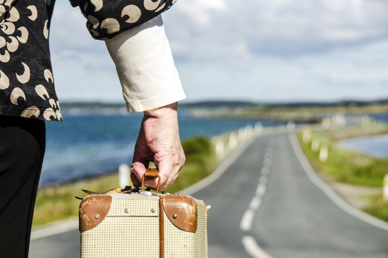 senior hand holding suitcase facing coastal road