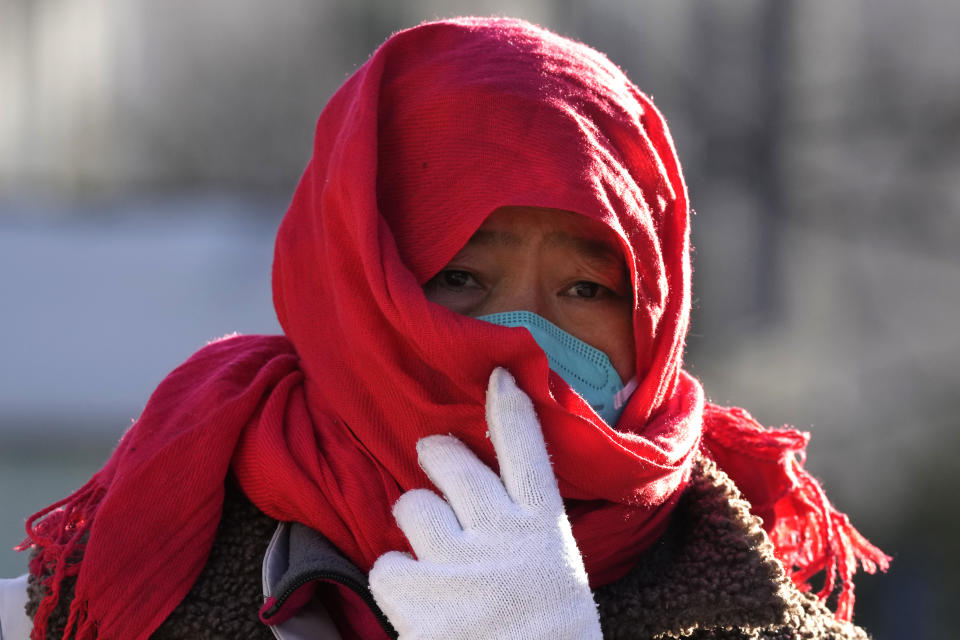 A worker adjusts her mask behind a scarf while working on the street of Beijing, Friday, Dec. 16, 2022. A week after China dramatically eased some of the world's strictest COVID-19 containment measures, uncertainty remained Thursday over the direction of the pandemic in the world's most populous nation. (AP Photo/Ng Han Guan)