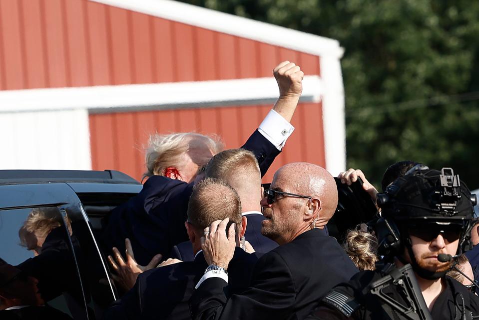 Republican presidential candidate former President Donald Trump pumps his fist as he is rushed into a car following a fatal shooting at his campaign rally.