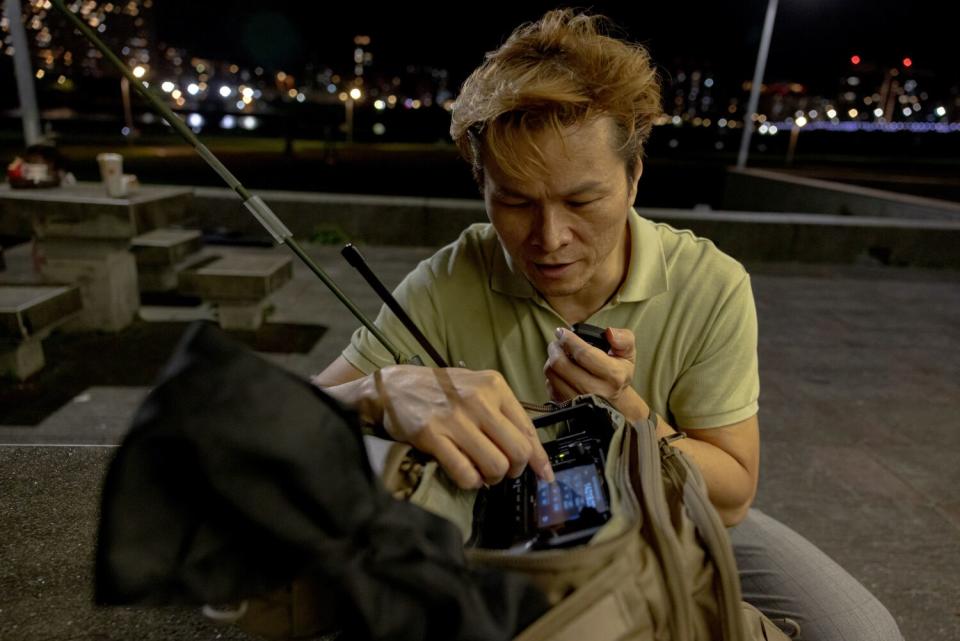 A man looks down while holding a radio unit in a bag