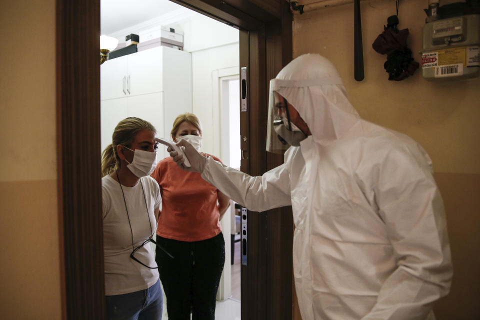 In this Friday, May 15, 2020 photo, a contact tracer with Turkey's Health Ministry's coronavirus contact tracing team, clad in white protective gear, mask and face shield, swabs Betul Sahbas, 47, left, who had been experiencing COVID-19 symptoms, to take a sample at her home in Istanbul. Thousands of tracers are going house to house nationwide to test and inform patients on isolation. Sahbaz, started showing symptoms after her flatmate tested positive. "I was scared and panicked, sure we hear about it, but it's different when you experience it" she explained. People who test positive are required by law to self-quarantine and are tracked by a phone application. (AP Photo/Emrah Gurel)