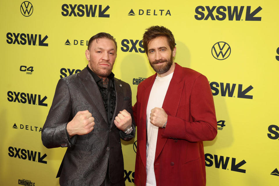 Conor Mcgregor and Jake Gyllenhaal posing against a photowall at SXSW promoting their new movie Road House