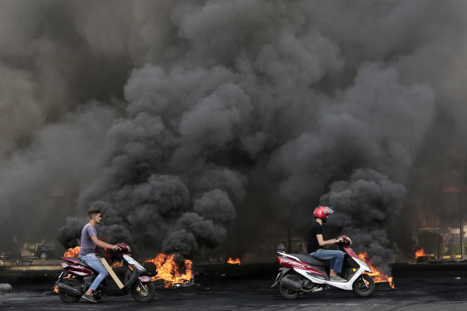 Men on scooters pass tires that were set on fire to block a road during a protest against government's plans to impose new taxes in Beirut, Lebanon, Friday, Oct. 18, 2019. The protests erupted over the government's plan to impose new taxes during a severe economic crisis, with people taking their anger out on politicians they accuse of corruption and decades of mismanagement. (AP Photo/Hassan Ammar)