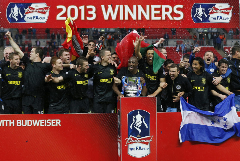 FILE - In this Saturday, May 11, 2013 file photo, Wigan Athletic's players celebrate with their trophy after their win against Manchester City at the end of their English FA Cup final soccer match at Wembley Stadium, London, Saturday, May 11, 2013. Wigan Athletic hadn’t won a piece of major silverware in its 81-year history until last May, when it pulled off one of the great FA Cup upsets by beating big-spending Manchester City in the final. Now, despite dropping out of the Premier League at the end of last season, it is on course to retain the famous trophy against all the odds. (AP Photo/Matt Dunham, File)