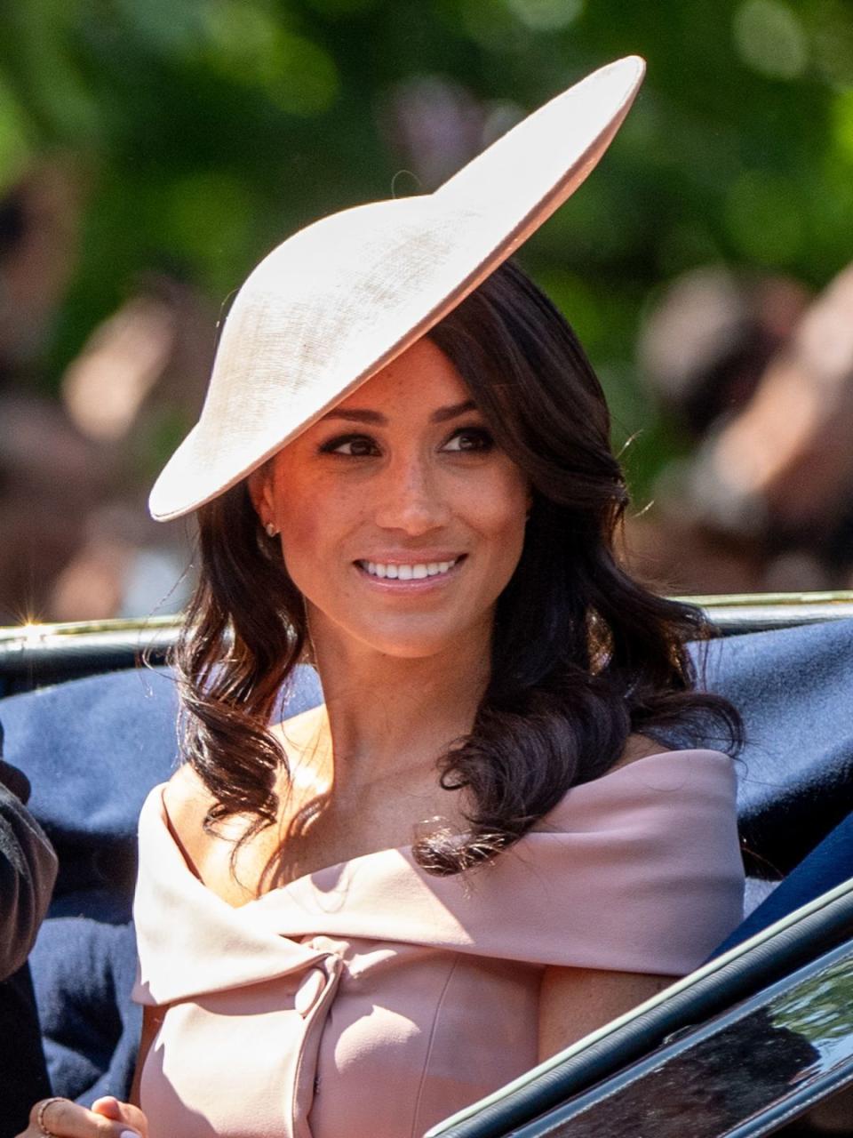 Meghan with curly hair and a sculptural hat in 2018