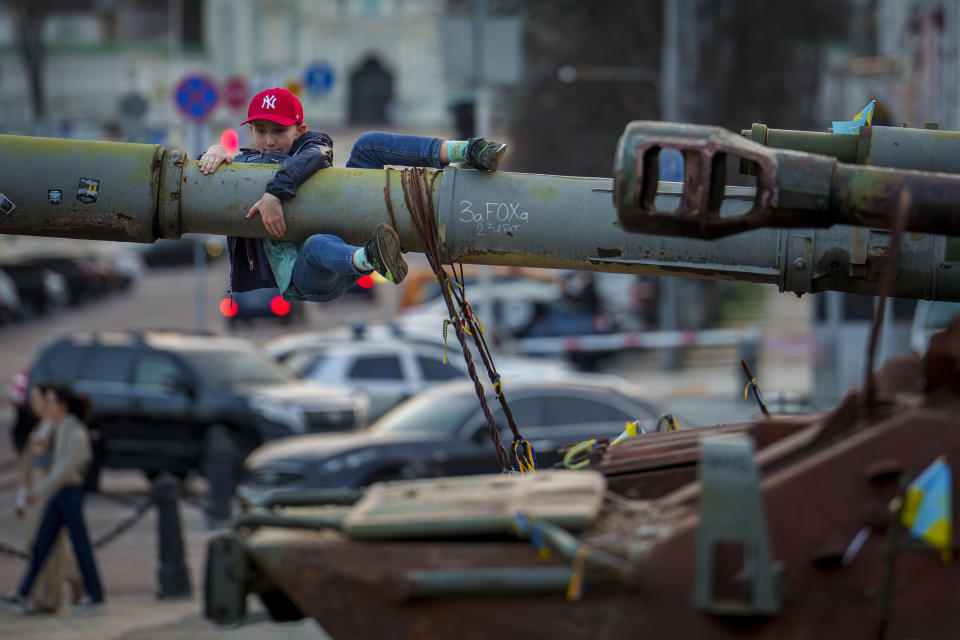 Un niño se cuelga del cañón de un tanque expuesto junto con otro equipamiento militar ruso destruido, en Kiev, Ucrania, el domingo 31 de marzo de 2024. (AP Foto/Vadim Ghirda)