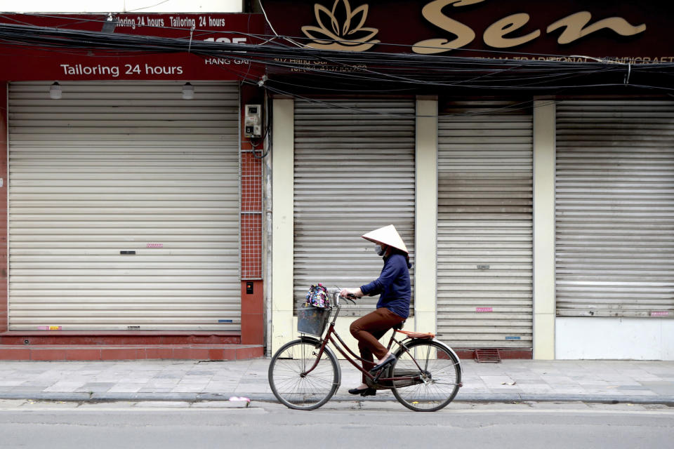 A woman cycles past closed shops in Hanoi, Vietnam, Friday, March 27, 2020. Vietnam's Prime Minister Nguyen Xuan Phuc has ordered to shut down non-essential business to curb the spread of COVID-19. The new coronavirus causes mild or moderate symptoms for most people, but for some, especially older adults and people with existing health problems, it can cause more severe illness or death. (AP Photo/Hau Dinh)