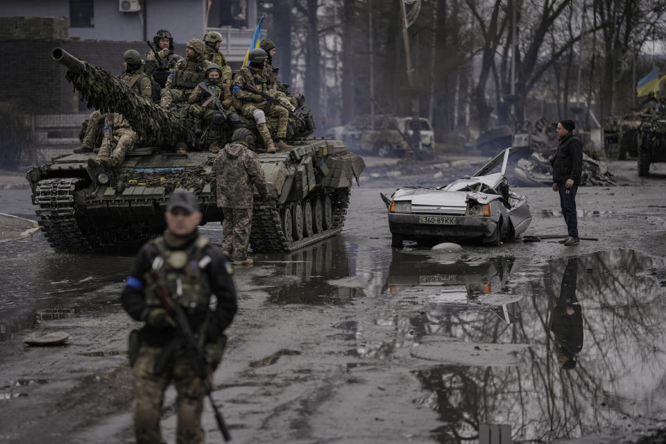 A man stands next to a civilian vehicle that was destroyed during fighting between Ukrainian and Russian forces that still contains the dead body of the driver as Ukrainian servicemen ride on a tank vehicle, outside Kyiv, Ukraine, Saturday, April 2, 2022. As Russian forces pull back from Ukraine's capital region, retreating troops are creating a "catastrophic" situation for civilians by leaving mines around homes, abandoned equipment and "even the bodies of those killed," President Volodymyr Zelenskyy warned Saturday.(AP Photo/Vadim Ghirda)