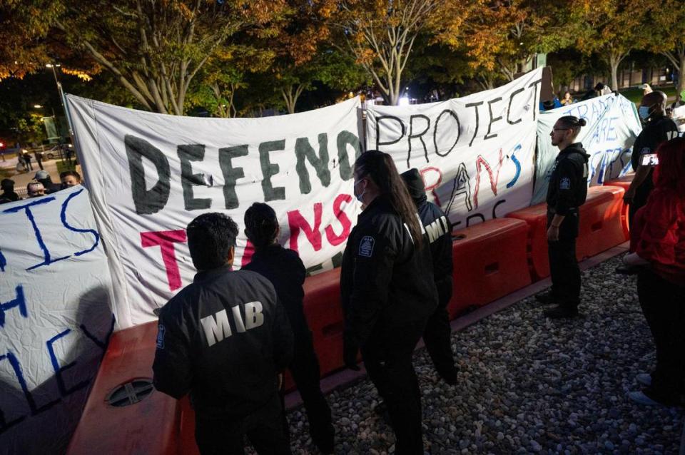 Protesters defending trans youth hold signs against a barricade protected by security outside the conference centers at UC Davis as speaker Riley Gaines, known for her outspoken views against trans-women in sports, prepares to speak Friday during her Speak Louder Campus Tour.
