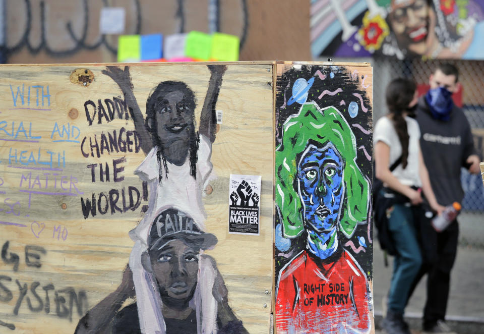 Two people walk past art-covered blockades Sunday, June 21, 2020, in Seattle, where streets are blocked off in what has been named the Capitol Hill Occupied Protest zone. Police pulled back from several blocks of the city's Capitol Hill neighborhood near the Police Department's East Precinct building earlier in the month after clashes with people protesting the death of George Floyd, a Black man who died after being restrained by Minneapolis police officers on May 25. (AP Photo/Elaine Thompson)